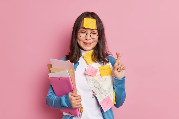 긍정적 인 여학생은 시험에 행운이 있다고 믿고 시험에 쓰인 둥근 안경에 종이와 스티커 메모를 붙인 정보를 기억하기 위해 침대를 만듭니다. 학생은 치트 시트를 사용합니다.