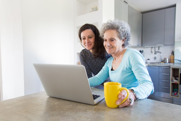 Signora senior positiva che mostra le foto alla figlia sul computer portatile