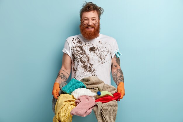 Позитивный улыбающийся бородатый мужчина рад почти закончить работу по дому, имеет грязную одежду