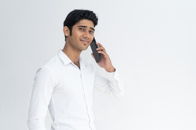 Положительный улыбающийся индийский парень, выступая на мобильном телефоне.