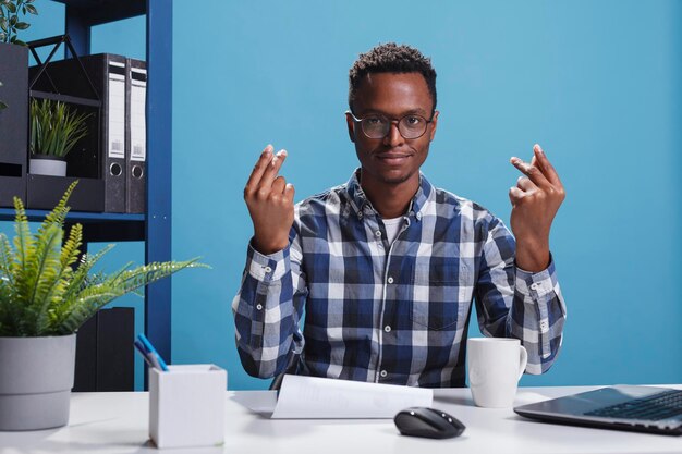 Positive smiling marketing company office employee making cash gesture while requesting payday money. Young adult finance department team leader making money symbol with fingers while in workspace.