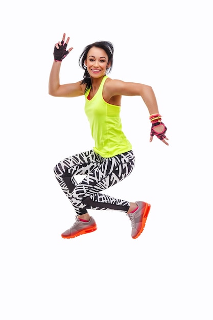 Positive smiling sporty female in green sportswear jumping. Isolated on white background.