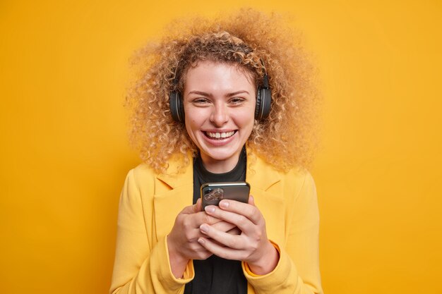ポジティブな笑顔の若い巻き毛の女性は、携帯電話のチェックを保持しています。