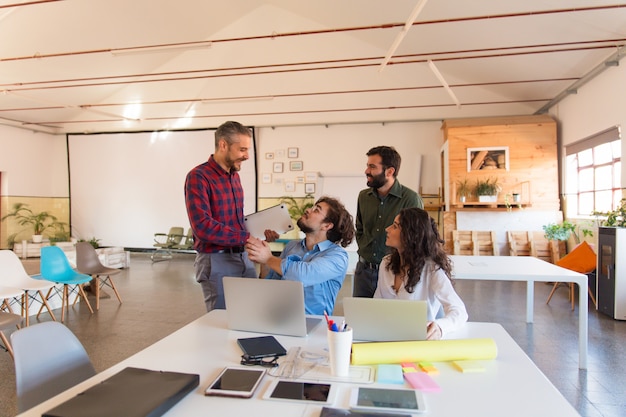 Positive startup group with laptops chatting in meeting room