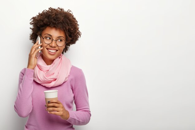 Positive student talks with interest and joy via cellular, feels timid to receive compliment, wears silk scarf and purple turtleneck sweater, enjoys drinking aromatic espresso