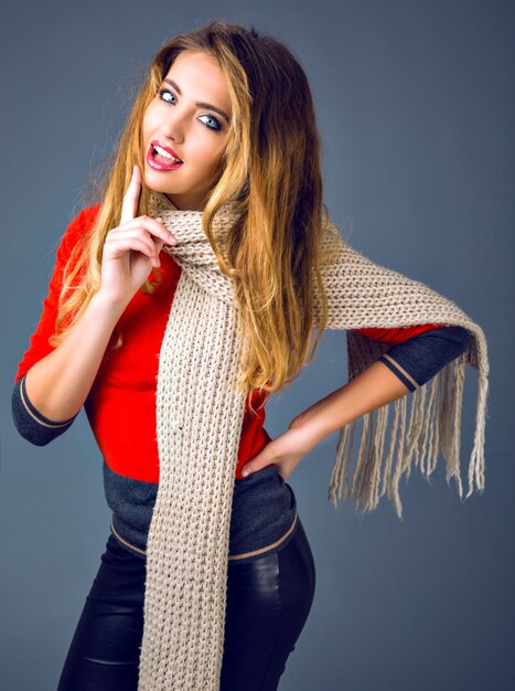 Позитивный портрет осенней зимы образа жизни студии моды, жизнерадостная белокурая женщина, играющая со своим шарфом, элегантная повседневная одежда.