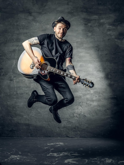 Positive stylish blues and jazz guitar player in a jump over grey background.