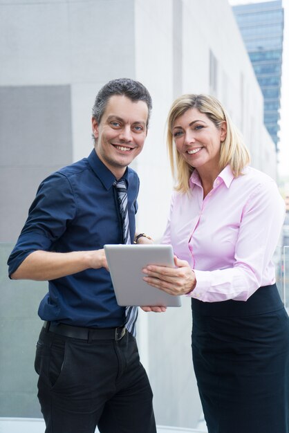 Positive successful business specialists discussing plan while using tablet outdoors.