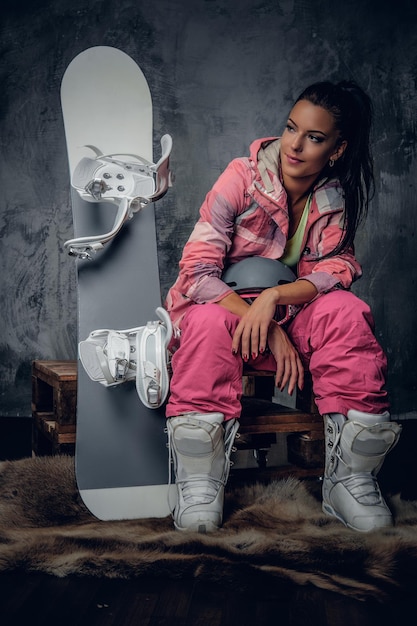 Positive suntanned sporty female posing with snowboard in a studio.