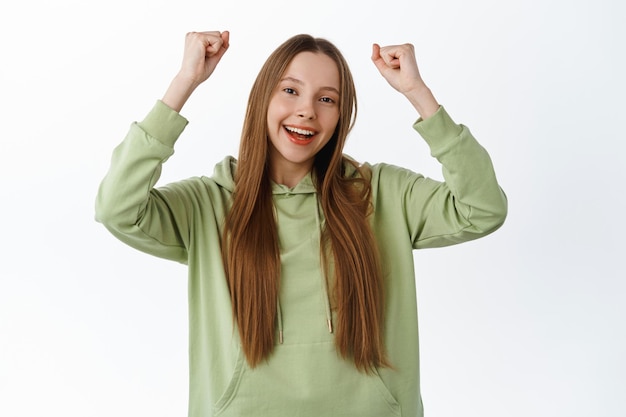 Positive supportive girl encourage you to keep up, boost confidence, fist pump and say yes, rooting for friend, celebrating, chanting happily, standing in hoodie against white background