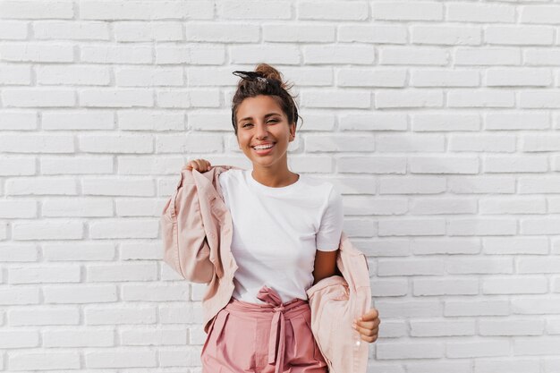 Positive tanned woman in white T-shirt puts on pink jacket