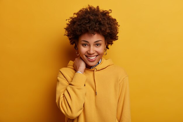 Positive teenage woman smiles happily, touches neck