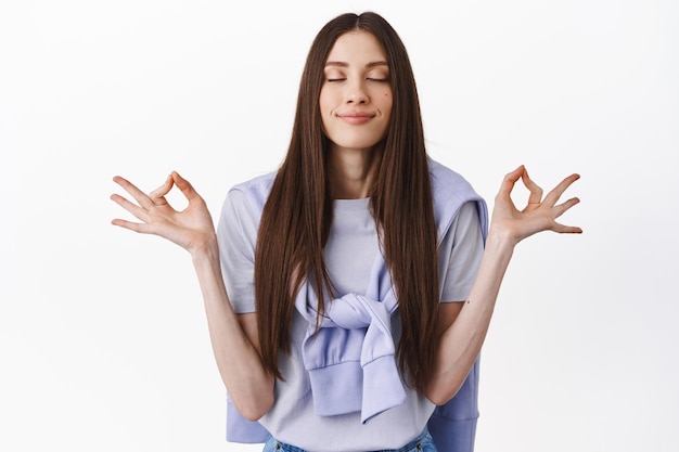 Foto gratuita solo pensieri positivi. sorridente giovane donna meditando, pratica yoga con gli occhi chiusi, respirando calmo e rilassato, riposando, avendo la pace in mente, in piedi su sfondo bianco