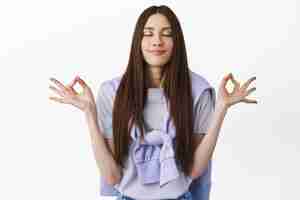 Free photo positive thoughts only. smiling young woman meditating, practice yoga with closed eyes, breathing calm and relaxed, resting, having peace in mind, standing over white background