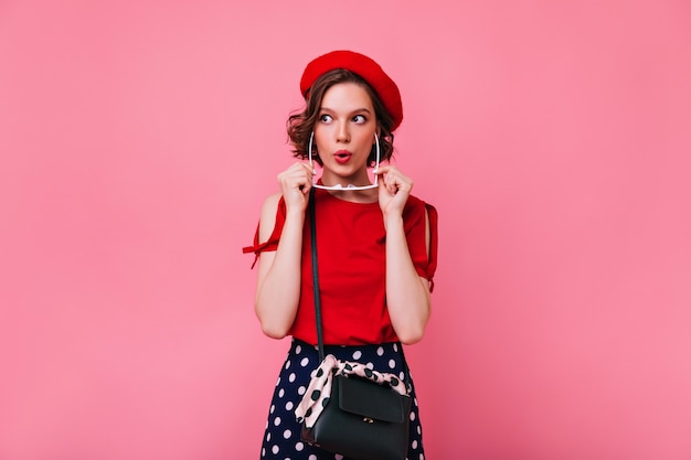Foto gratuita ragazza bianca positiva in berretto rosso carino che esprime interesse. foto interna di modella francese disinvolta con taglio di capelli corto.