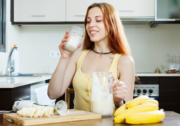 Положительная женщина, пьющая молочный коктейль с бананами