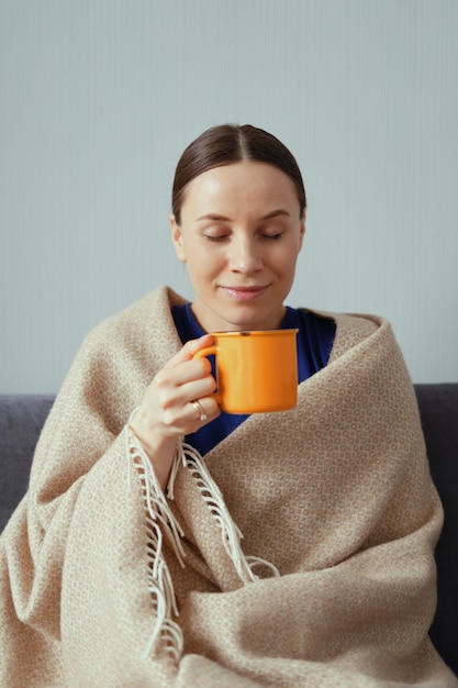 Free photo positive woman enjoying a cup of tea wrapped in a blanket