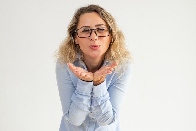 Positive woman in glasses puckering lips and blowing air kiss