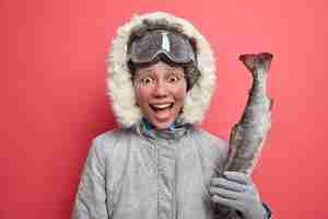 Foto gratuita la donna positiva va a pescare durante il periodo invernale vestito con una giacca calda, indossa occhiali da snowboard e ha riposo attivo durante la bassa temperatura.