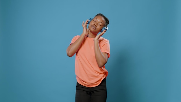 Positive woman having fun with headphones and rhythm, dancing in front of camera with eyes closed. cheerful person listening to music on headset and doing dance moves over isolated background