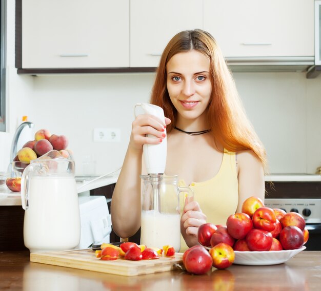 Positive woman making beverages with nectarines and milk