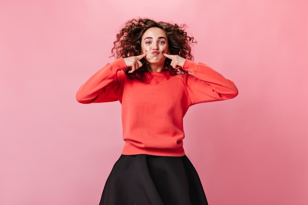 Positive woman in orange sweatshirt makes funny face on pink background