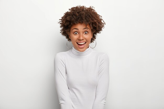 ポジティブな女性は心地よく笑顔で、シルバーのイヤリングとカジュアルなタートルネックのセーターを着ています