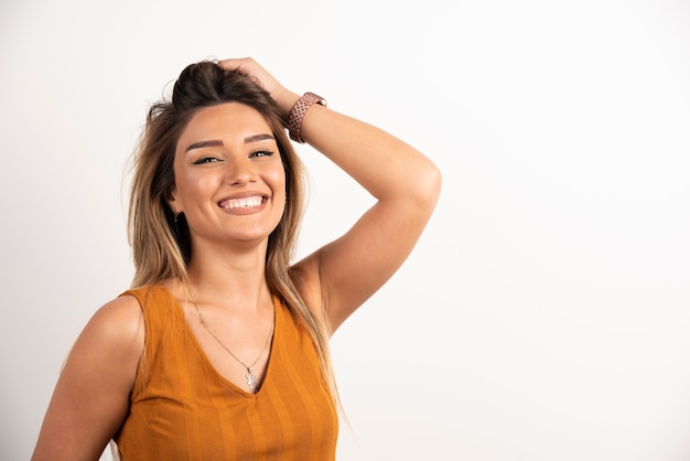 Donna positiva che si tocca i capelli e posa su sfondo bianco.