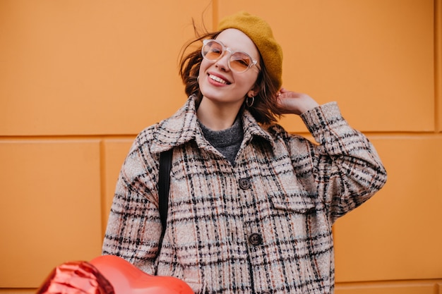 Foto gratuita donna positiva in cappotto di tweed con sorriso in posa sulla parete arancione