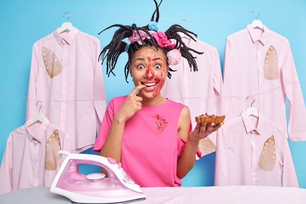 Positive woman with dreadlocks enjoys eating tasty pie has face