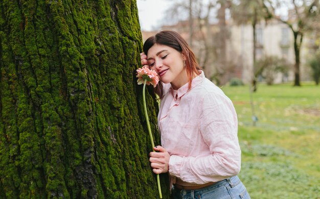 공원에서 나무 근처 꽃과 긍정적 인 여자