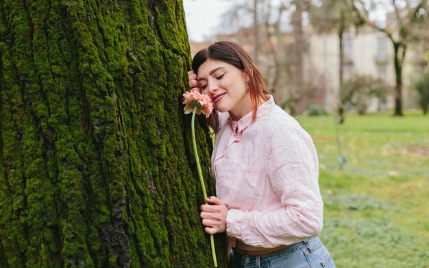 Positive woman with flower near tree in park