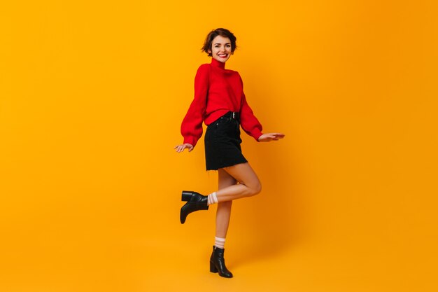 Positive woman with short hair dancing on yellow wall