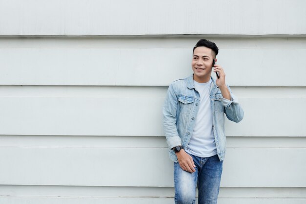 Premium Photo | Positive young asian man in casual outfit leaning on  building wall and having phone conversation