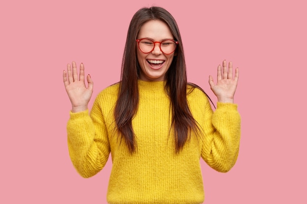 Positive young Asian woman with overjoyed expression, shows palms, giggles at funny joke