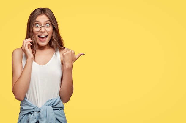 Positive young brunette with glasses posing against the yellow wall