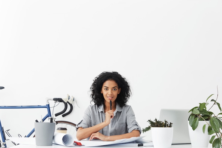 Free Photo positive young dark-skinned female engineer touching lips with pen