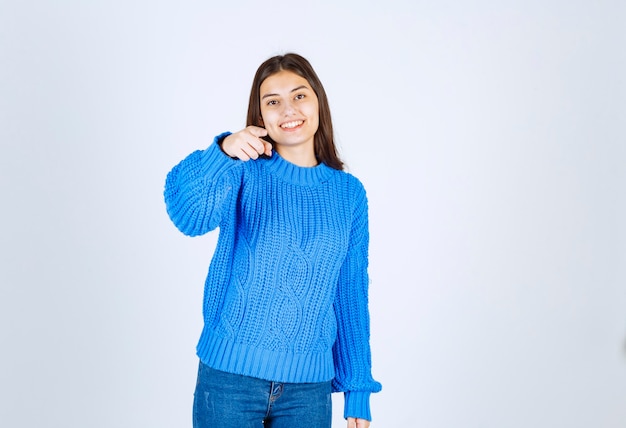 positive young girl model pointing forward on pink wall.