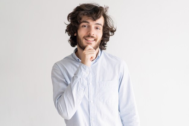 Positive young man touching chin and looking at camera