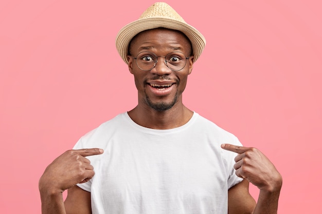 Positive young man with satisfied expression, advertises new casual t shirt