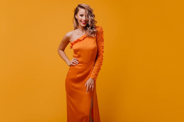 Positive young woman in bright long dress smiling in studio