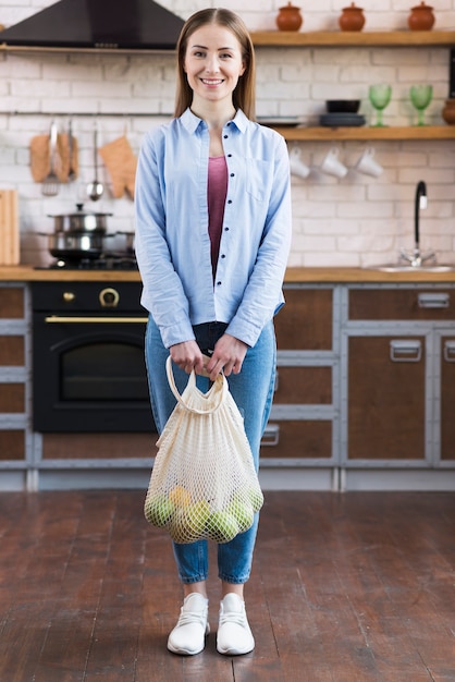 Foto gratuita giovane donna positiva che tiene borsa riutilizzabile con i frutti