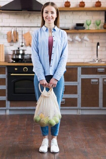 果物と再利用可能なバッグを保持している肯定的な若い女性