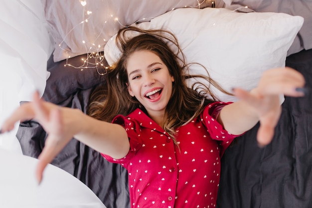 Positive young woman posing with happy face expression early in morning. Charming caucasian girl having fun in bed before sleep.