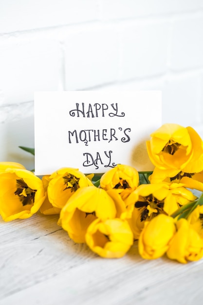 Postcard Mother's Day and yellow tulips on a light wooden background , holiday concept