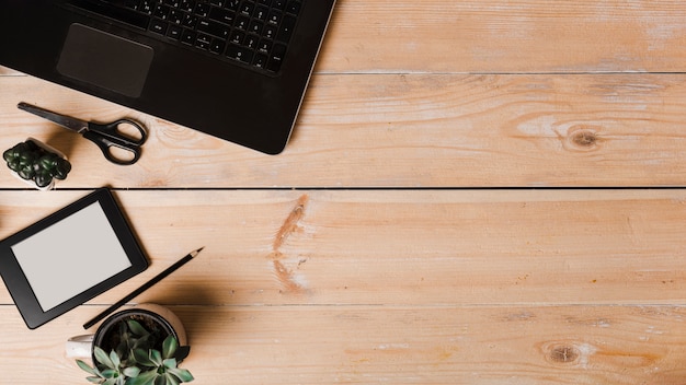 Free photo pot plants; scissor; pencil; ebook reader and laptop on wooden background