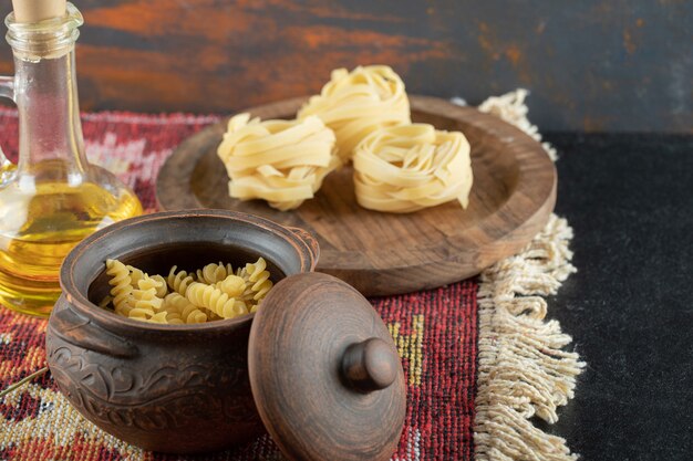 A pot of raw spiral macaroni with uncooked rolled pasta on wooden board
