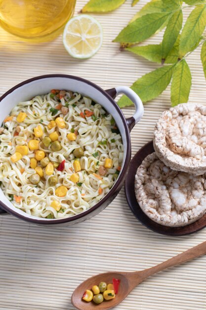 A pot of tasty noodles with corns, peas and round bread crusts 