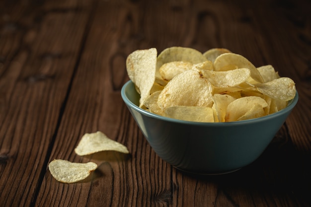 Potato chips in bowl on a wooden table.