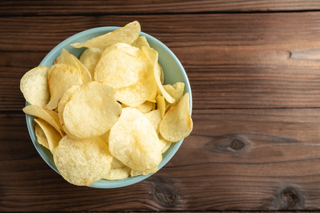 Potato chips in bowl on a wooden table.
